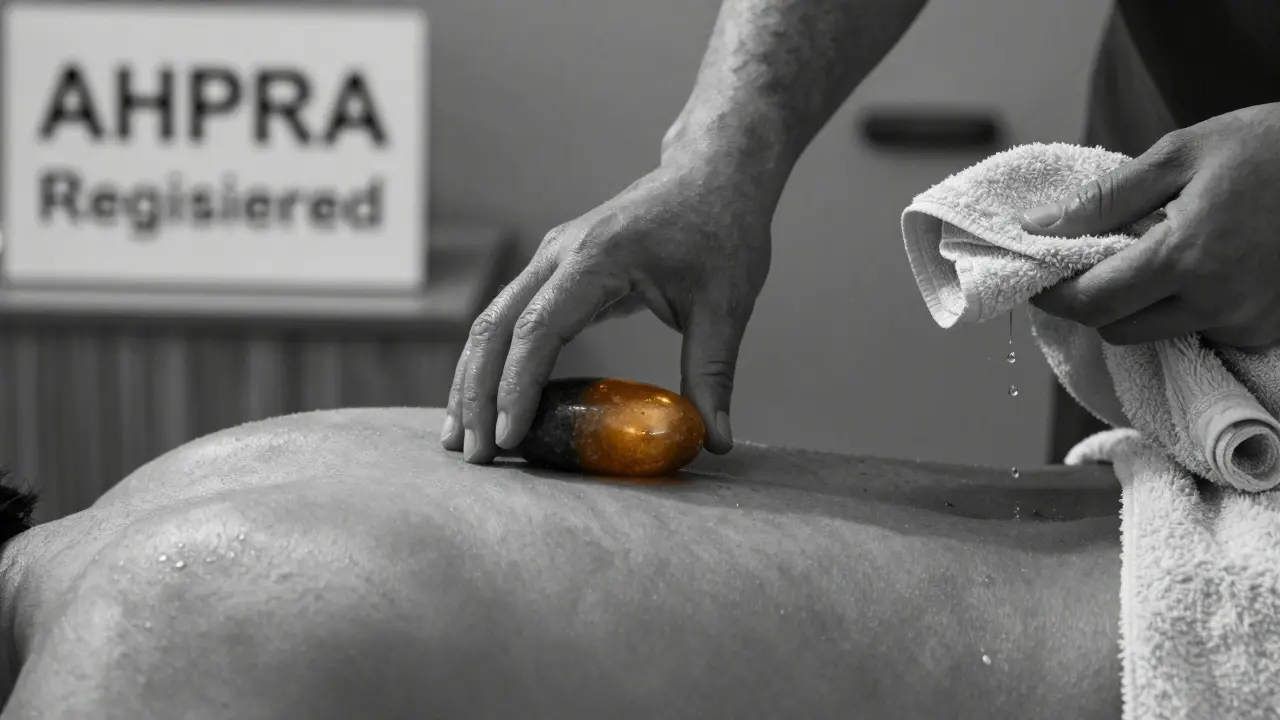 Close-up of hands placing a warm stone on a back, with a towel and wooden floor in soft focus.